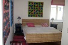 Schlafzimmer mit Doppelbett aus Korbgeflecht, Nachttischen und bunten Wandbildern.
