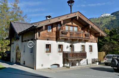 Ploderhaus Appartement Wilder Kaiser Alpines Wohnhaus mit weißer Fassade, Holzbalkonen und Satteldach vor bewaldeten Bergen.