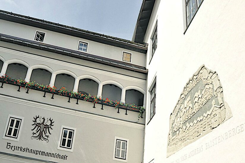 Graffito Ein historisches Gebäude mit kunstvollen Fenstern und Blumenkästen. An der Wand ist ein dekoratives Relief zu sehen.