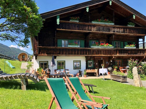 Ein Garten voller Träume Ein traditionelles Holzhaus mit Garten und Liegen. Die Umgebung ist grün und sonnig, ideal für Entspannung.