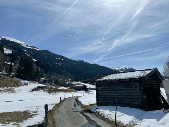 Verschneite Berglandschaft mit einem asphaltierten Weg und einer Holzhütte im Vordergrund.