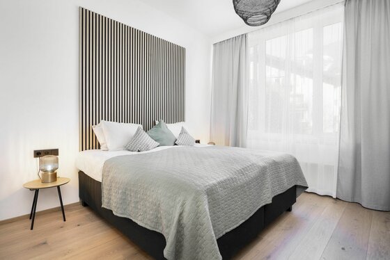 Schlafzimmer im Apartment 1919 Modernes Doppelbett mit gestreiftem Wandpaneel aus Holz, Nachttisch und großem Fenster.