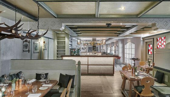 Innenansicht eines Restaurants mit Holztischen, einer zentralen Bar und dekorativem Hirschgeweih an der Decke.