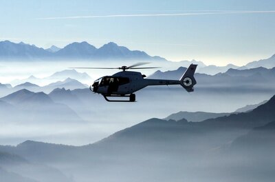 Kitz-Air Ein Hubschrauber schwebt über einer beeindruckenden Berglandschaft. Der Himmel ist klar und die Berge sind von Nebel umgeben.
