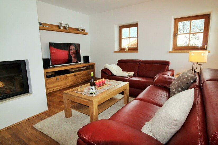 Wohnzimmer mit roter Ledercouch, Holztisch, Fernseher und Kamin.