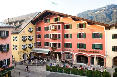 Blick auf den Hotel-Gasthof Tiefenbrunner mit Außengastronomie auf einem gepflasterten Platz in Kitzbühel.