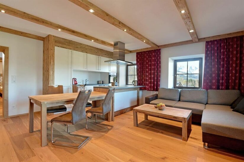 Wohnzimmer-Küche im Pöllhof Moderner Wohn- und Essbereich mit Holzboden, Holzbalkendecke, Ecksofa und offener Küche.