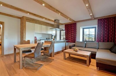 Moderner Wohn- und Essbereich mit Holzboden, Holzbalkendecke, Ecksofa und offener Küche.