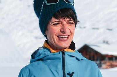 Doris Ritter - Bikeguide Porträt einer Frau in blauer Outdoorjacke und Strickmütze vor verschneitem Berghang.