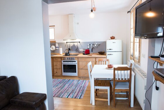 Küche mit Holzfronten, weißem Esstisch, Retro-Kühlschrank und TV-Gerät an der Wand.