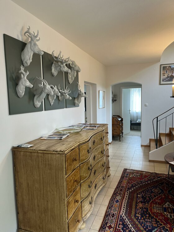 Innenansicht eines Flurs mit Holzkommode, Teppich und weißen Tierskulpturen an der Wand.