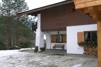 Alpines Wohnhaus mit weißer Fassade, Holzverkleidung und einer Bank vor dem Eingang im Schnee.