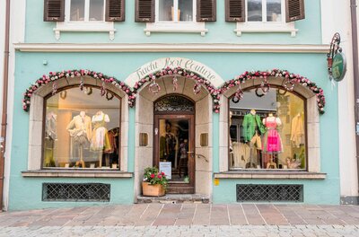 Trachten Eder Ladengeschäft Fassade eines Trachtengeschäfts mit Schaufenstern, die Dirndl und Lederhosen auf Puppen zeigen.