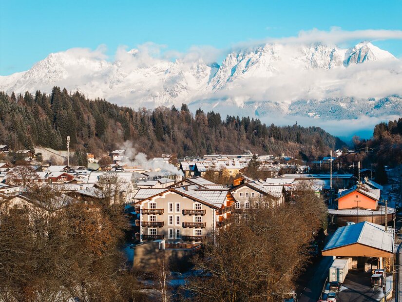 Winteransicht Kitzbühel mit Wildem Kaiser Blick über verschneite Hausdächer in Kitzbühel auf das schneebedeckte Massiv des Wilden Kaisers unter blauem Himmel.