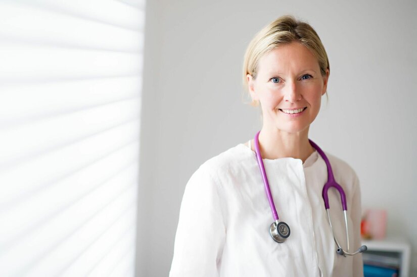 Dr. med. univ. Beate Obermoser Porträt einer Ärztin in weißer Kleidung mit einem lila Stethoskop um den Hals vor hellem Hintergrund.