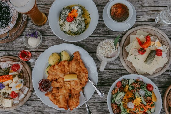 Seidlalm Essen Verschiedene Speisen wie Schnitzel, Knödel, Salat und Brotzeitplatten auf einem Holztisch aus der Vogelperspektive.