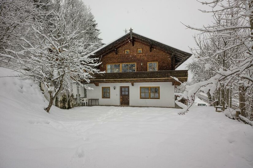 Haus Wetti in Jochberg Zweistöckiges Holzhaus mit weißem Erdgeschoss in einer verschneiten Winterlandschaft.
