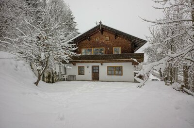 Haus Wetti in Jochberg Zweistöckiges Holzhaus mit weißem Erdgeschoss in einer verschneiten Winterlandschaft.