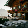 Ein rustikales Holzhaus mit blühenden Balkonkästen und einer einladenden Terrasse, umgeben von Bergen im Hintergrund.