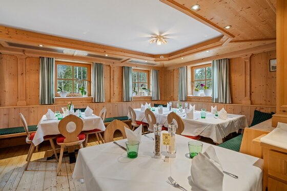 Rustikale Gaststube mit holzgetäfelten Wänden, eingedeckten Tischen und Eckbänken.