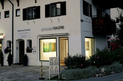 Ein Gebäude mit der Aufschrift „Galerie“ auf der Vorderseite. Es befindet sich in einer malerischen Umgebung mit Blumen und einem klaren Himmel.