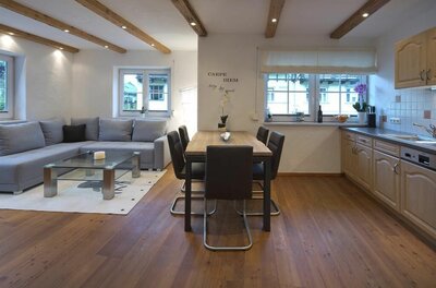 Moderner Wohn- und Essbereich mit grauem Ecksofa, Holztisch und Küchenzeile in einer Ferienwohnung.