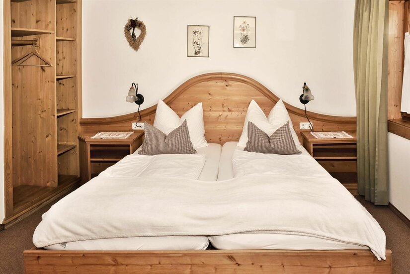 Schlafzimmer im Mühlbergerhof Doppelbett aus hellem Holz mit weißer Bettwäsche, Nachttischen und einem offenen Holzschrank in einem Pensionszimmer.