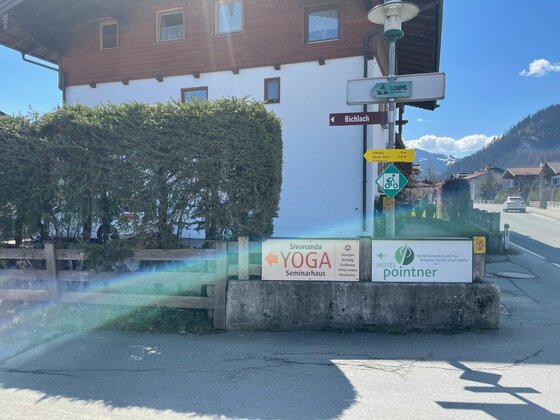 Wegweiser für Wanderer und Radfahrer vor einem Gebäude mit Hinweisschildern für Yoga und eine Praxis.