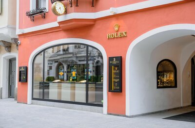 Juwelier Schroll Kitzbühel Außenansicht des Juweliergeschäfts Schroll in Kitzbühel mit lachsfarbener Fassade und Rolex-Logo.