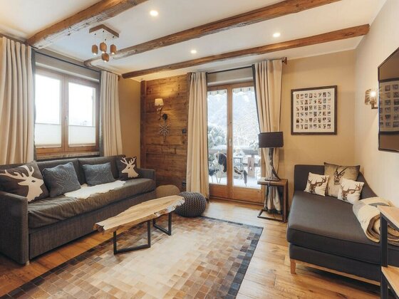 Wohnzimmer mit zwei grauen Sofas, Holztisch, Deckenbalken und Balkontür mit Blick auf verschneite Berge.