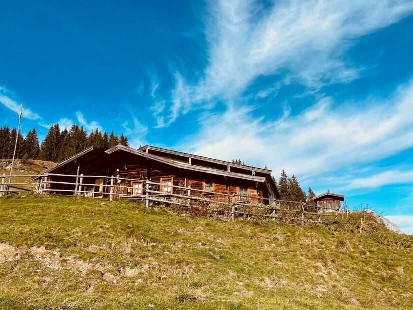 Hütte am Hollenauer Kreuz Rustikale Holzhütte mit Zaun auf einem Grashang unter blauem Himmel.