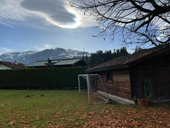 Garten mit Bergblick Garten mit Fußballtor und Holzhütte vor schneebedeckten Bergen unter bewölktem Himmel.
