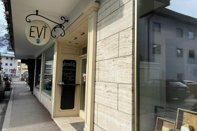 Evi Café und Feines Außenansicht des Cafés Evi mit einem runden Ladenschild und einer Menütafel an der hellen Fassade.