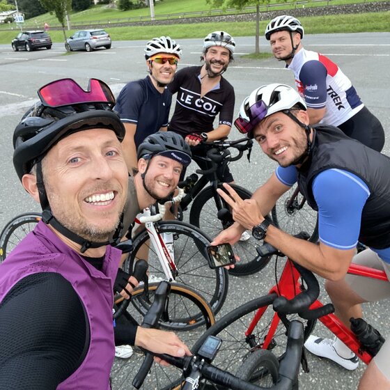We Ride Rennradgruppe Sechs Rennradfahrer mit Helmen und Sportbekleidung posieren für ein Selfie auf einem Parkplatz.