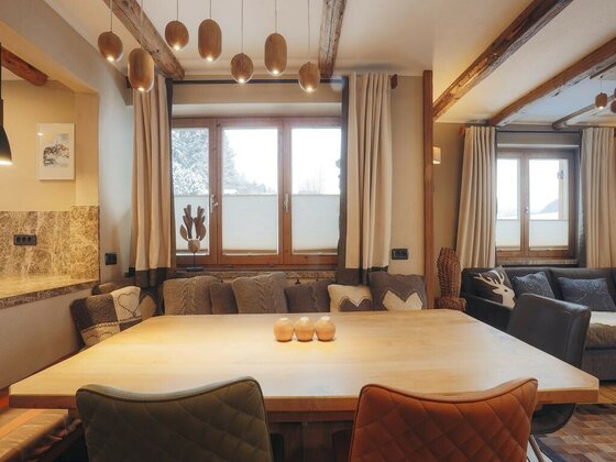 Moderner Essbereich mit Holztisch, gepolsterten Stühlen und hängenden Holzleuchten vor einem Fenster.