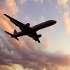 Ein Flugzeug fliegt hoch über den Himmel, umgeben von sanften, pastellfarbenen Wolken während des Sonnenuntergangs.