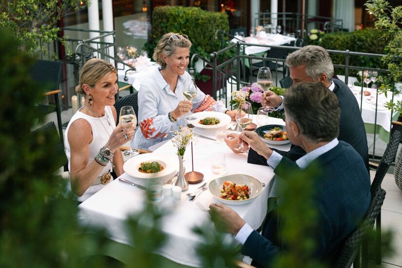 Restaurantterrasse Hotel Kaiserhof Kitzbühel Vier Personen beim Abendessen auf einer Restaurantterrasse mit Weingläsern und Speisen.