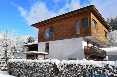 Apartment Achenweg Außenansicht Modernes zweistöckiges Gebäude mit Holzfassade im Obergeschoss und schneebedeckter Hecke im Vordergrund.