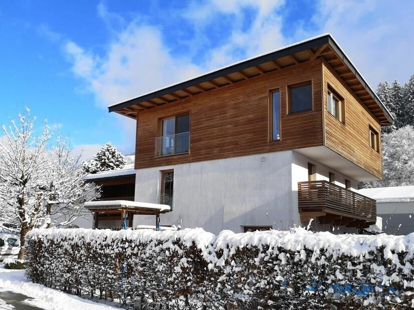 Modernes zweistöckiges Gebäude mit Holzfassade im Obergeschoss und schneebedeckter Hecke im Vordergrund.
