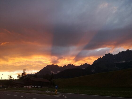 Silhouette eines gezackten Gebirgsmassivs vor einem orange-violett gefärbten Abendhimmel mit Wolkenstrahlen.