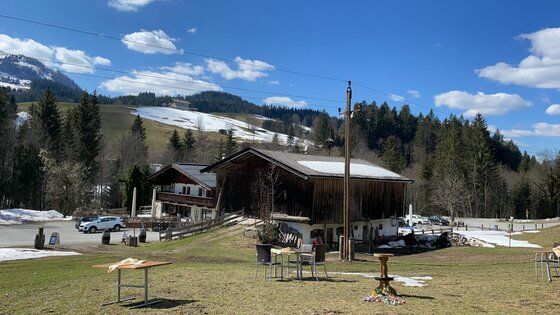 Gasthof Eiserne Hand Alpiner Gasthof aus Holz vor bewaldeten Bergen mit Schneeresten unter blauem Himmel.