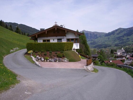 Alpines Wohnhaus an einer asphaltierten Kurve mit Blick auf ein Dorf im Tal und bewaldete Berge.