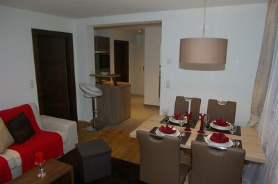 Moderner Wohn- und Essbereich mit gedecktem Holztisch, Sofa mit roter Decke und Blick in die Küche.