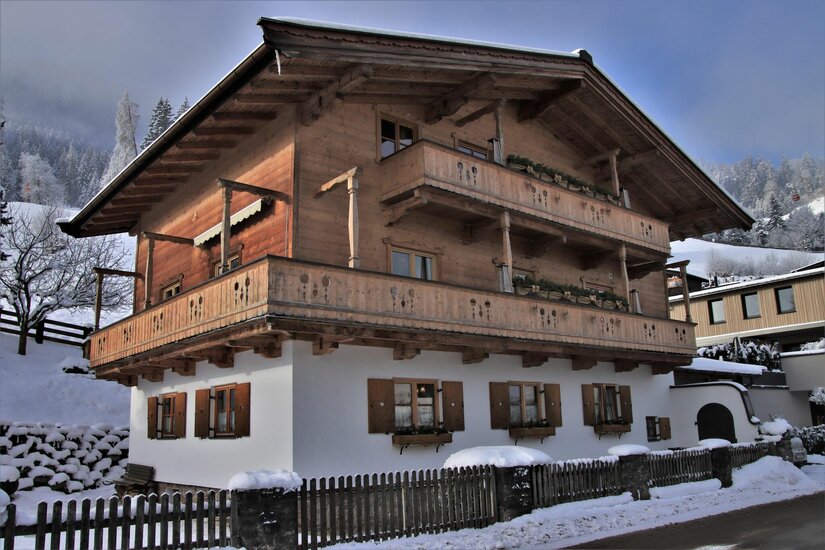 Haus Obernauer im Winter Zweistöckiges Alpenhaus mit Holzfassade, Balkonen und weißem Erdgeschoss in verschneiter Landschaft.