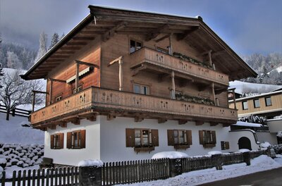 Zweistöckiges Alpenhaus mit Holzfassade, Balkonen und weißem Erdgeschoss in verschneiter Landschaft.