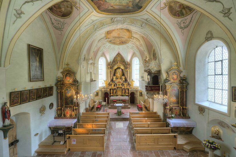 Eine schöne Kirche mit einem beeindruckenden Altar und kunstvollen Deckenmalereien. Die Holzbänke bieten Platz für die Besucher.