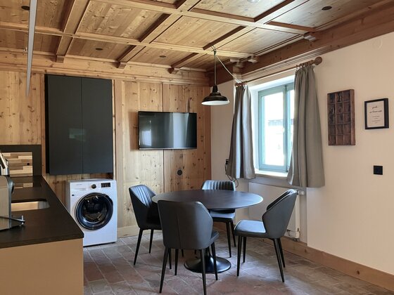 Ein gemütlicher Essbereich mit einem runden Tisch und Stühlen. Die Wände sind aus Holz, und es gibt moderne Annehmlichkeiten wie einen Fernseher und eine Waschmaschine.
