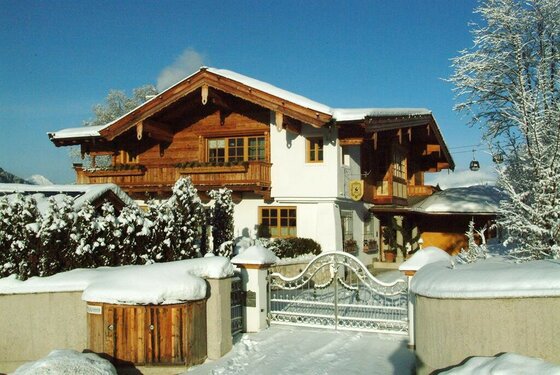 Alpines Wohnhaus mit Holzfassade und schneebedecktem Dach hinter einem weißen Metalltor im Winter.