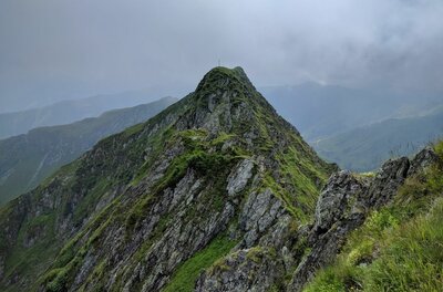 Gipfel des Kleinen Rettensteins Steiler, felsiger Berggipfel mit grünem Bewuchs unter bewölktem Himmel.