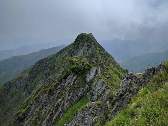 Gipfel des Kleinen Rettensteins Steiler, felsiger Berggipfel mit grünem Bewuchs unter bewölktem Himmel.